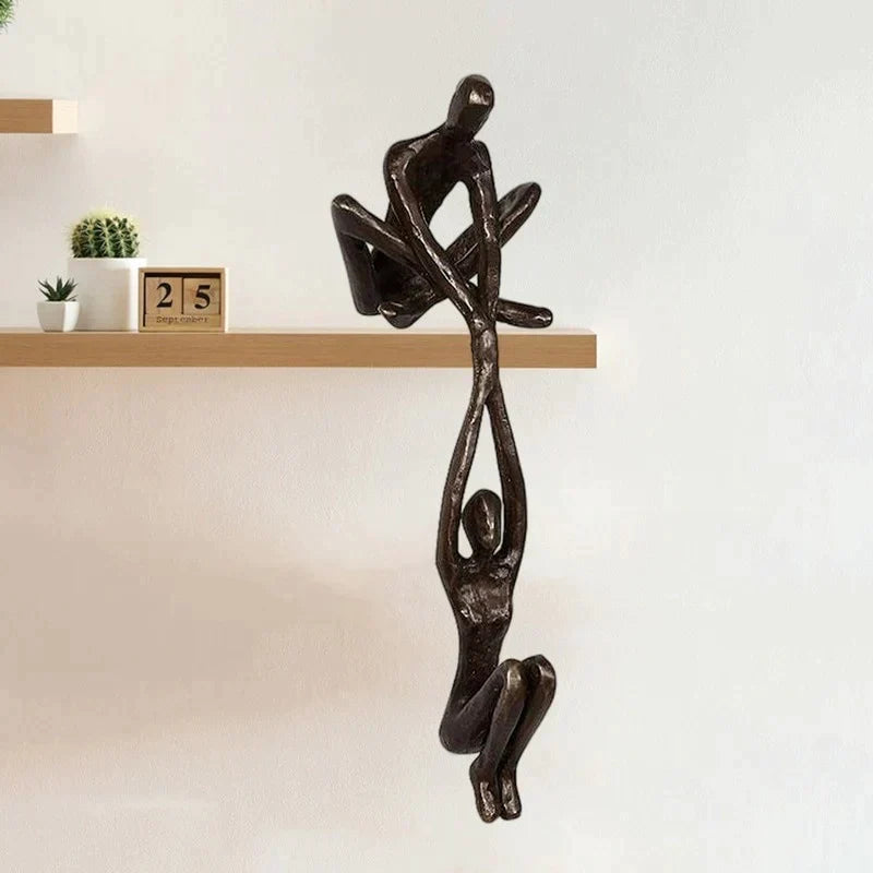 Black paired figure sculpture beside decorative objects on a wood shelf