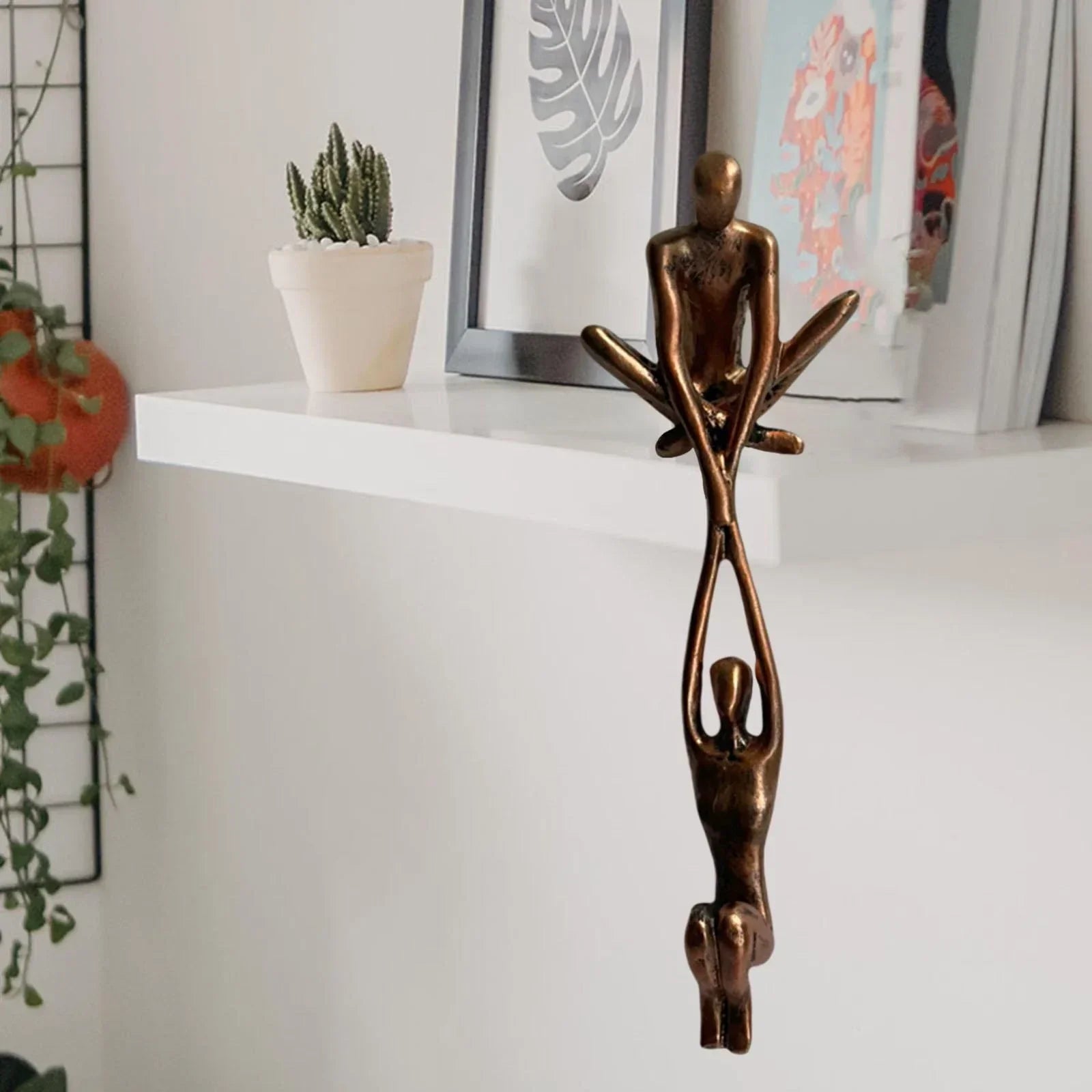 Bronze resin figures displayed on a white shelf with framed artwork