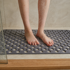 Non slip shower mat in gray beneath wet feet inside a bright tiled shower