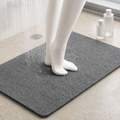 Loofah shower mat in gray beneath mannequin feet with water spraying nearby