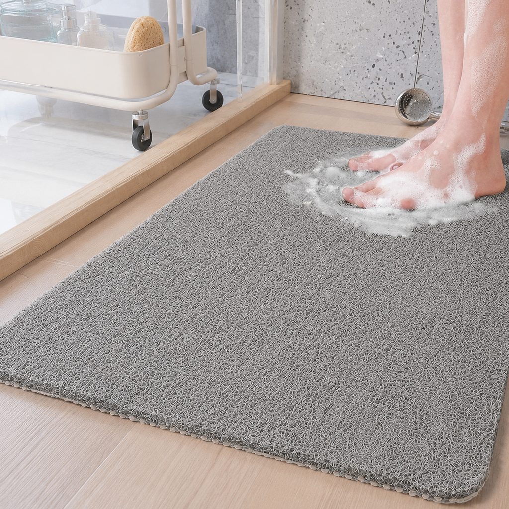 Loofah shower mat in gray beneath wet feet beside a glass shower partition