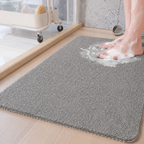 Loofah shower mat in gray beneath wet feet beside a glass shower partition