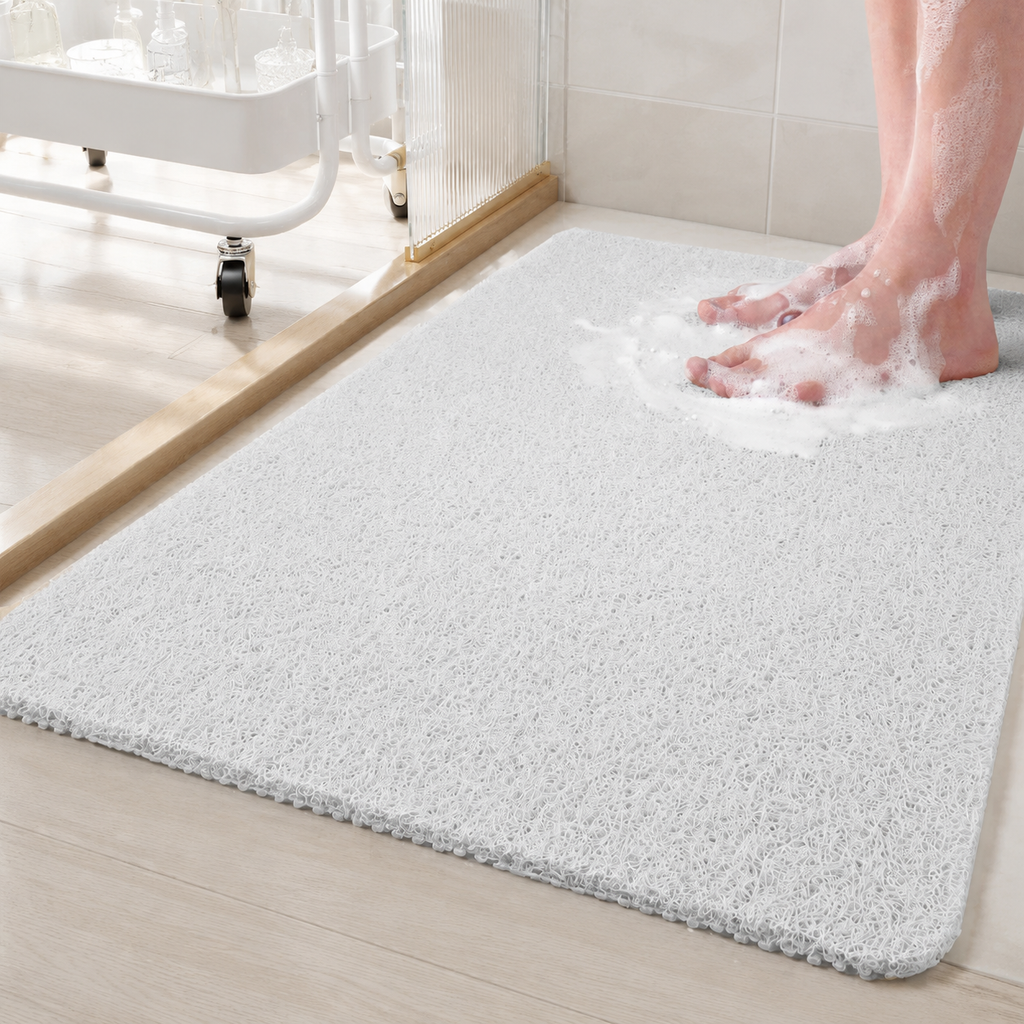 Loofah shower mat in white beneath wet feet beside a glass shower partition