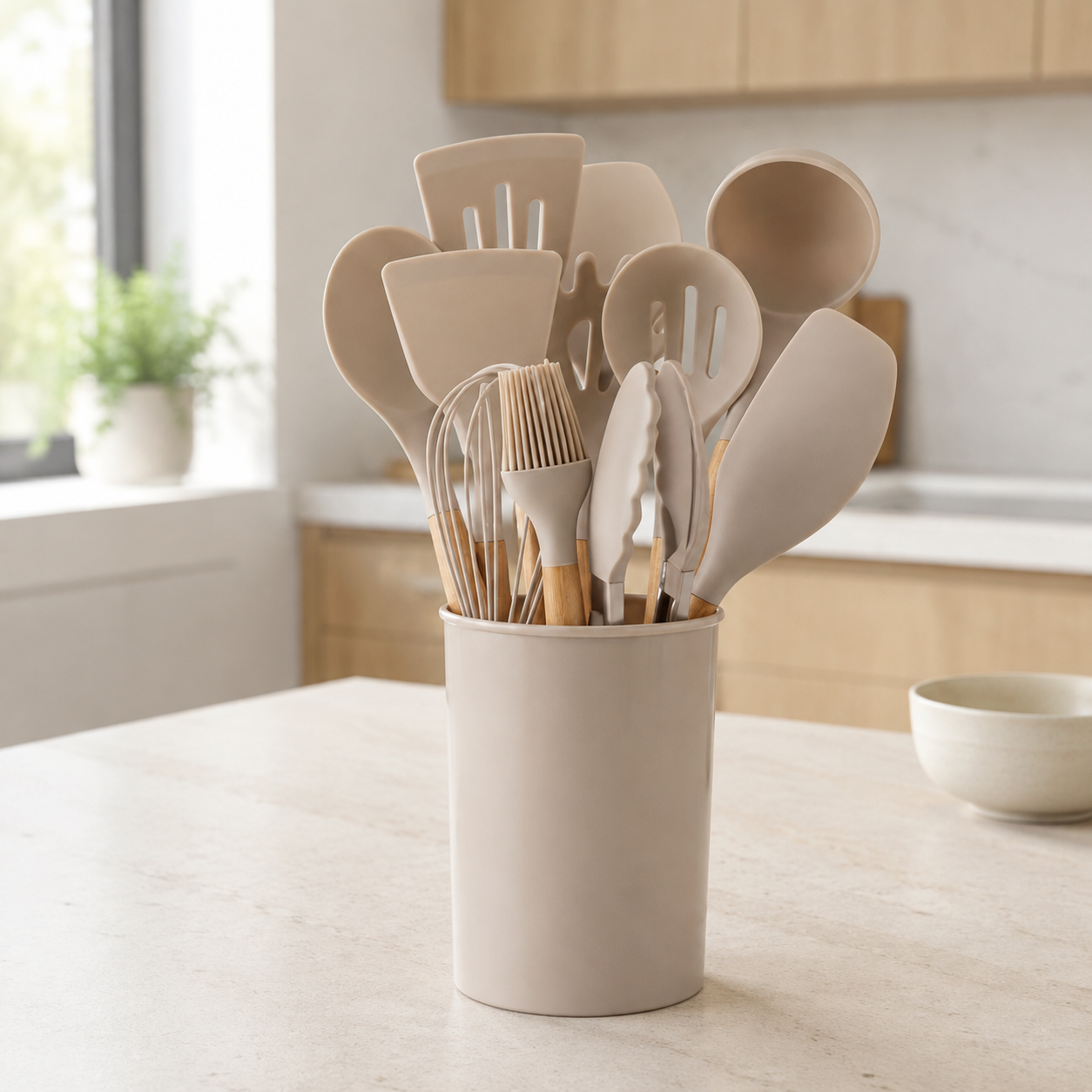 Beige silicone cooking utensil set stands in a matching holder on a bright kitchen island.