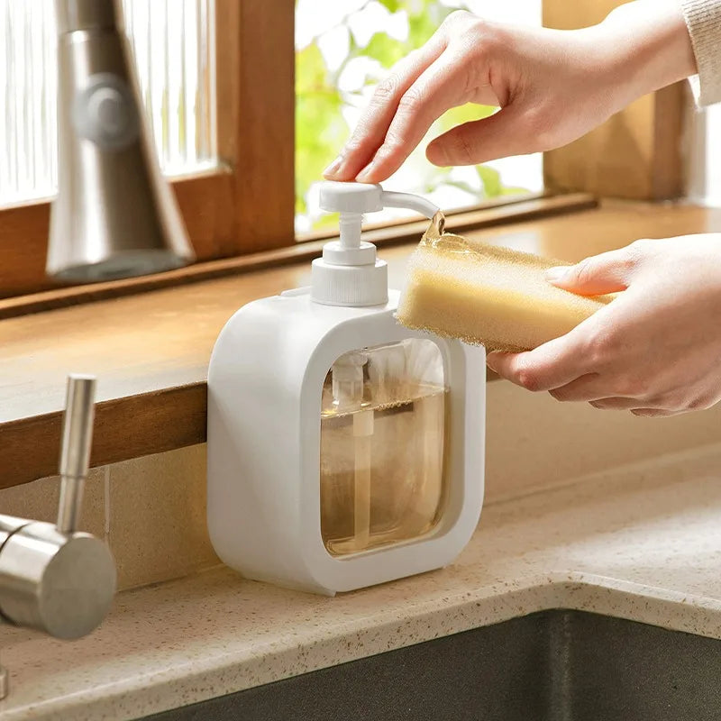 White soap dispenser being pressed above a kitchen sink.
