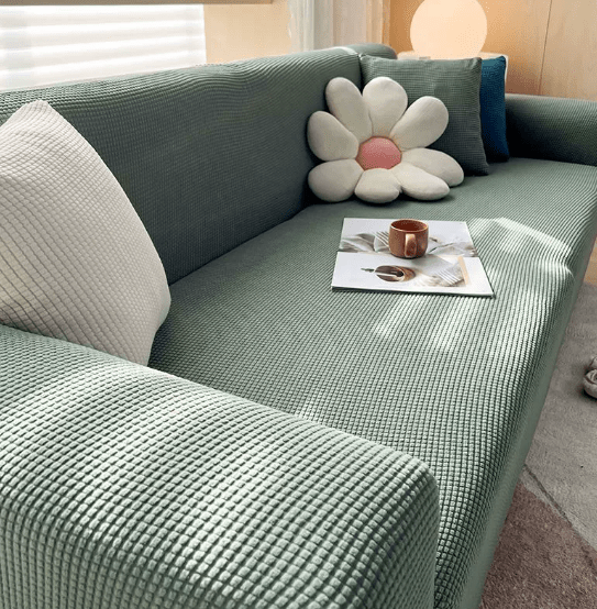 Sofa cover in green jacquard fitted over a sofa with flower cushion.