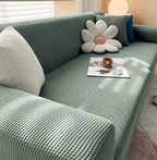 Sofa cover in green jacquard fitted over a sofa with flower cushion.