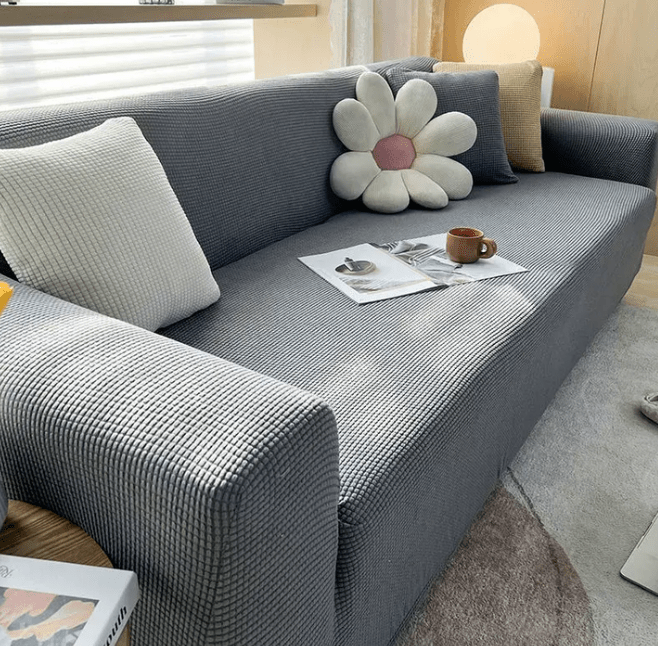 Sofa cover in dark gray jacquard fitted over a sofa with flower cushion.