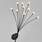 Solar-powered fiber optic string lights with multiple thin black wires ending in glowing warm white bulbs, mounted on a small black solar panel against a light gray background.
