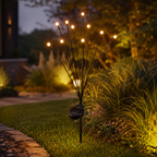 A solar-powered outdoor light fixture with multiple thin black branches ending in small warm yellow bulbs, mounted on a stake in a landscaped garden bed at night.
