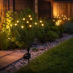 Solar garden light posts with multiple glowing warm-white globe bulbs mounted on thin black stems, placed in a landscaped yard beside a stone bed, grass, and wooden fence at night.