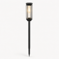 A modern black metal solar landscape light with a glass cylinder shade and a long stake, shown lit against a plain white background.