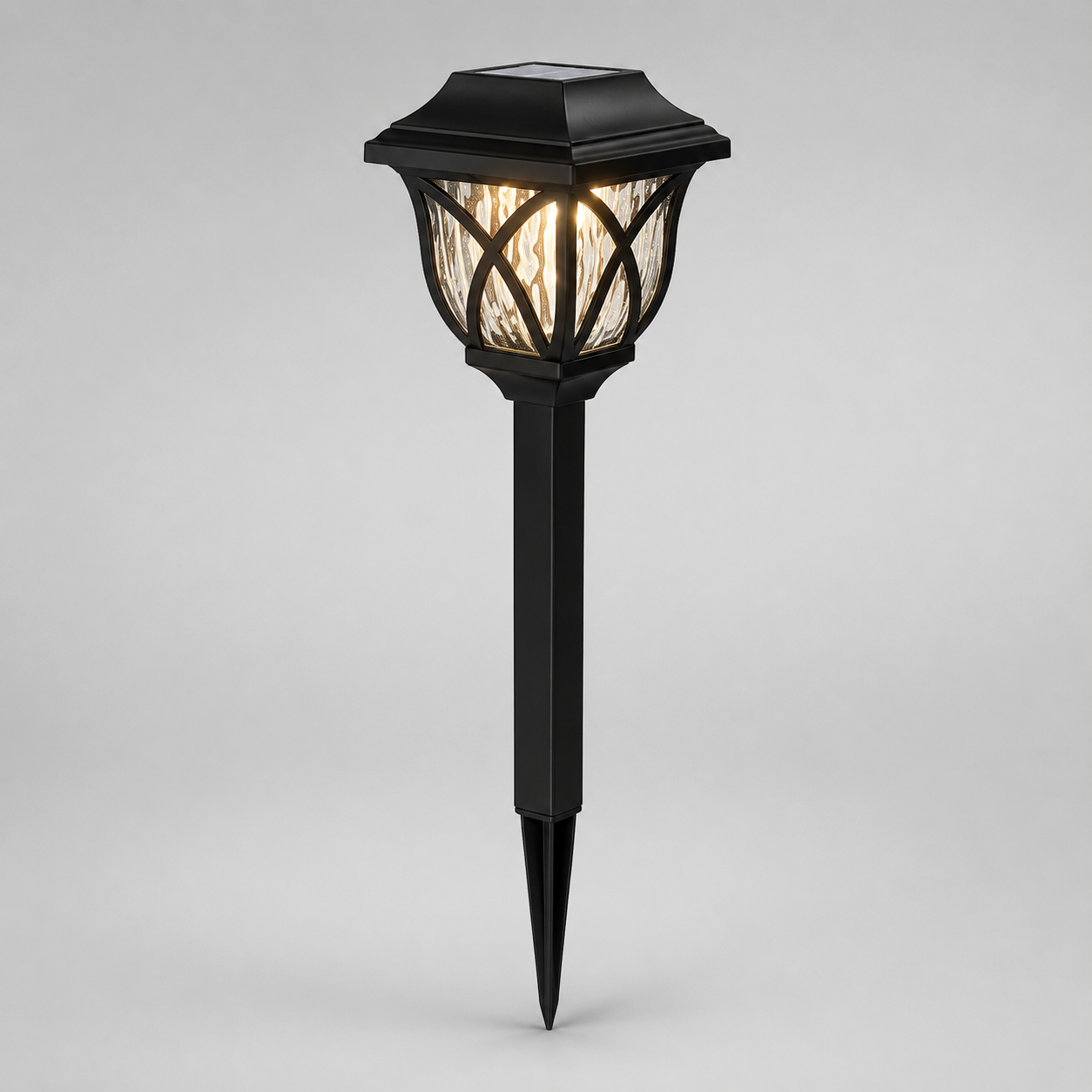 A black solar-powered outdoor landscape light with a pointed stake base and a textured glass shade, shown illuminated against a neutral gray background.