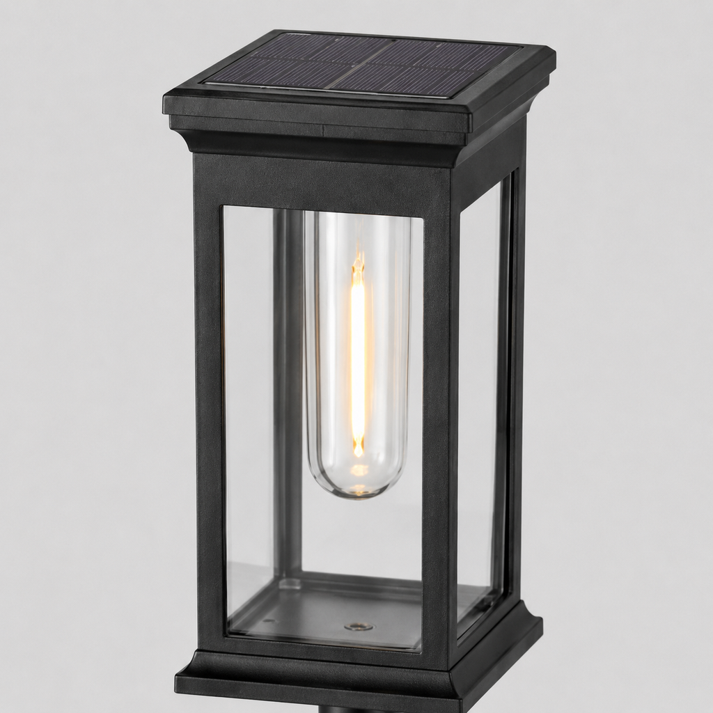 A modern solar-powered outdoor light fixture with a black metal frame, clear glass panels, and a glowing filament bulb inside, shown against a neutral light gray background.