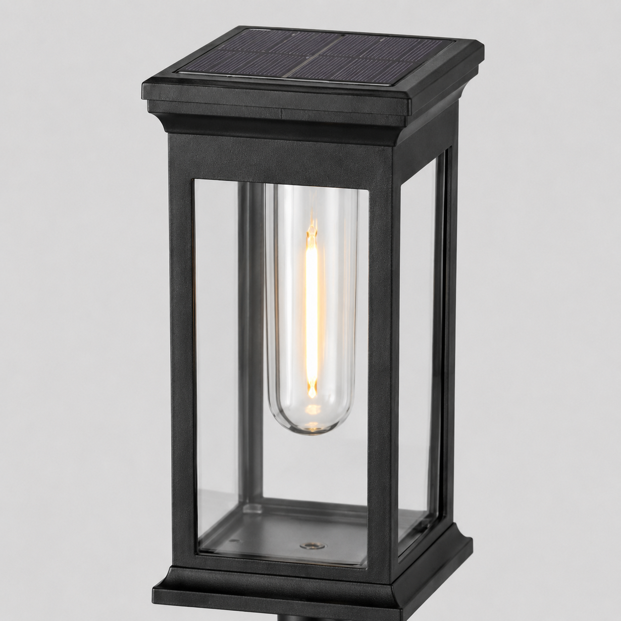 A modern solar-powered outdoor light fixture with a black metal frame, clear glass panels, and a glowing filament bulb inside, shown against a neutral light gray background.