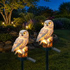 Two solar owl garden lights illuminating a landscaped garden at blue hour.