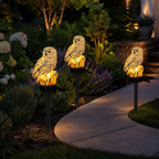 Three solar owl garden lights lining a curved pathway at night.