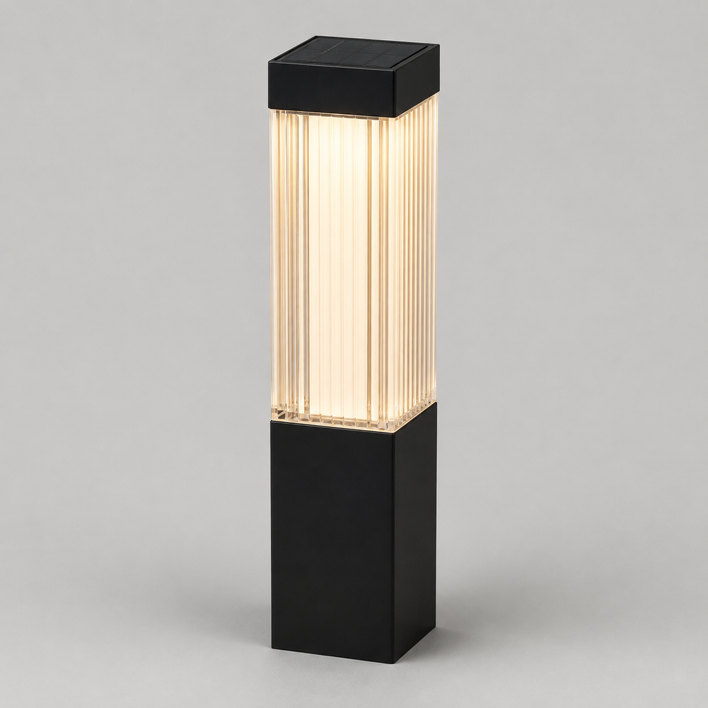 A modern outdoor bollard light with a matte black rectangular base and top cap, featuring a ribbed glass shade that glows with warm white light, shown against a neutral gray background.