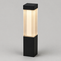 A modern outdoor bollard light with a matte black rectangular base and top cap, featuring a ribbed glass shade that glows with warm white light, shown against a neutral gray background.