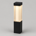 A modern outdoor bollard light with a matte black rectangular base and top cap, featuring a ribbed glass shade that glows with warm white light, shown against a neutral gray background.