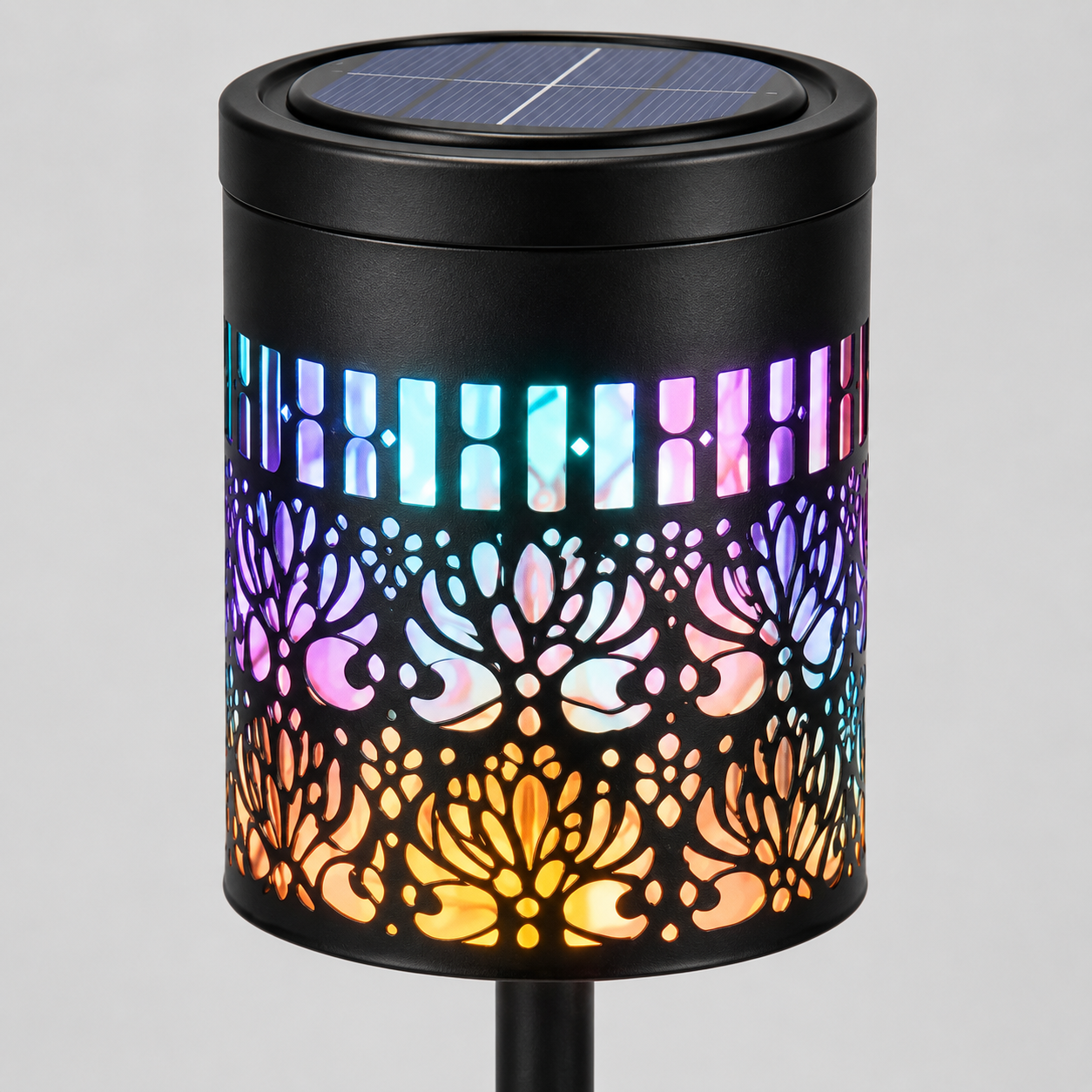 A black cylindrical solar-powered outdoor light with a colorful LED light-up pattern, featuring a floral cutout design that glows with pink, blue, purple, and orange hues, shown on a neutral gray background.
