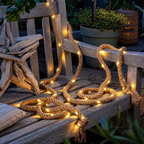 Solar rope lights loop across a weathered cedar bench beside planters at blue hour.