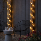 Solar rope lights wrap two patio posts beside black chairs and a concrete table.