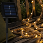 Solar rope lights rest beside a black solar panel on a weathered cedar bench.