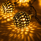 Solar string lights shown in a close-up of two glowing perforated globe shades and patterned shadows.