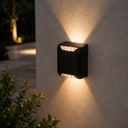 A modern black outdoor wall light fixture mounted on a textured beige stucco wall, casting warm light beams upward and downward at night.