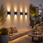 Five modern black rectangular wall sconces mounted on a beige wall, casting warm light beams downward on a rooftop patio at dusk with city skyline lights in the background.