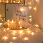 Star fairy lights decorate a tabletop beside candles and a framed print.