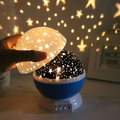 Blue star projector with its dome cover lifted and warm star shapes projected behind it.
