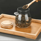Bamboo spoon lifting loose tea from an open glass storage jar
