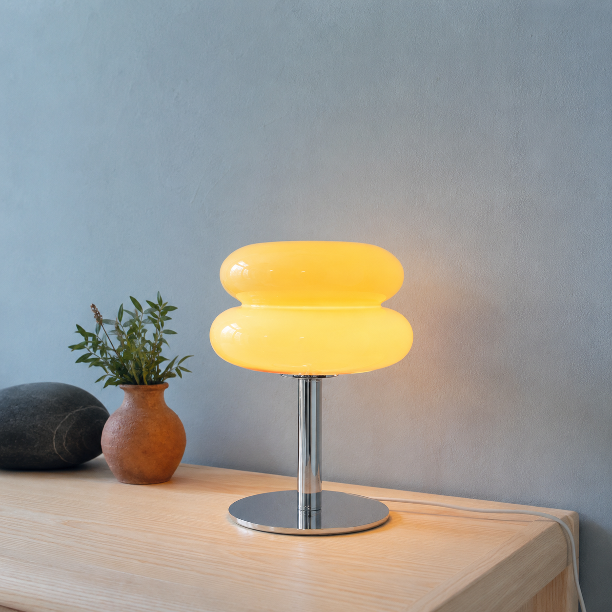Yellow sculptural glass table lamp glowing on a pale wood console.