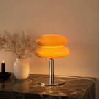 Orange sculptural glass table lamp glowing on a dark marble console.