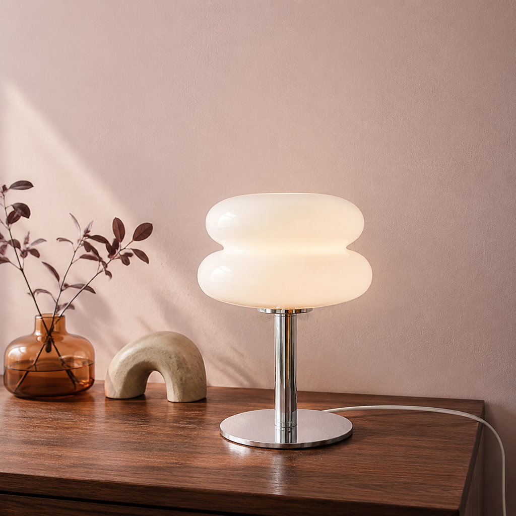 White sculptural glass table lamp glowing on a walnut console.