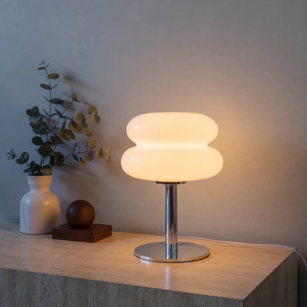 White sculptural glass table lamp glowing on a travertine console.