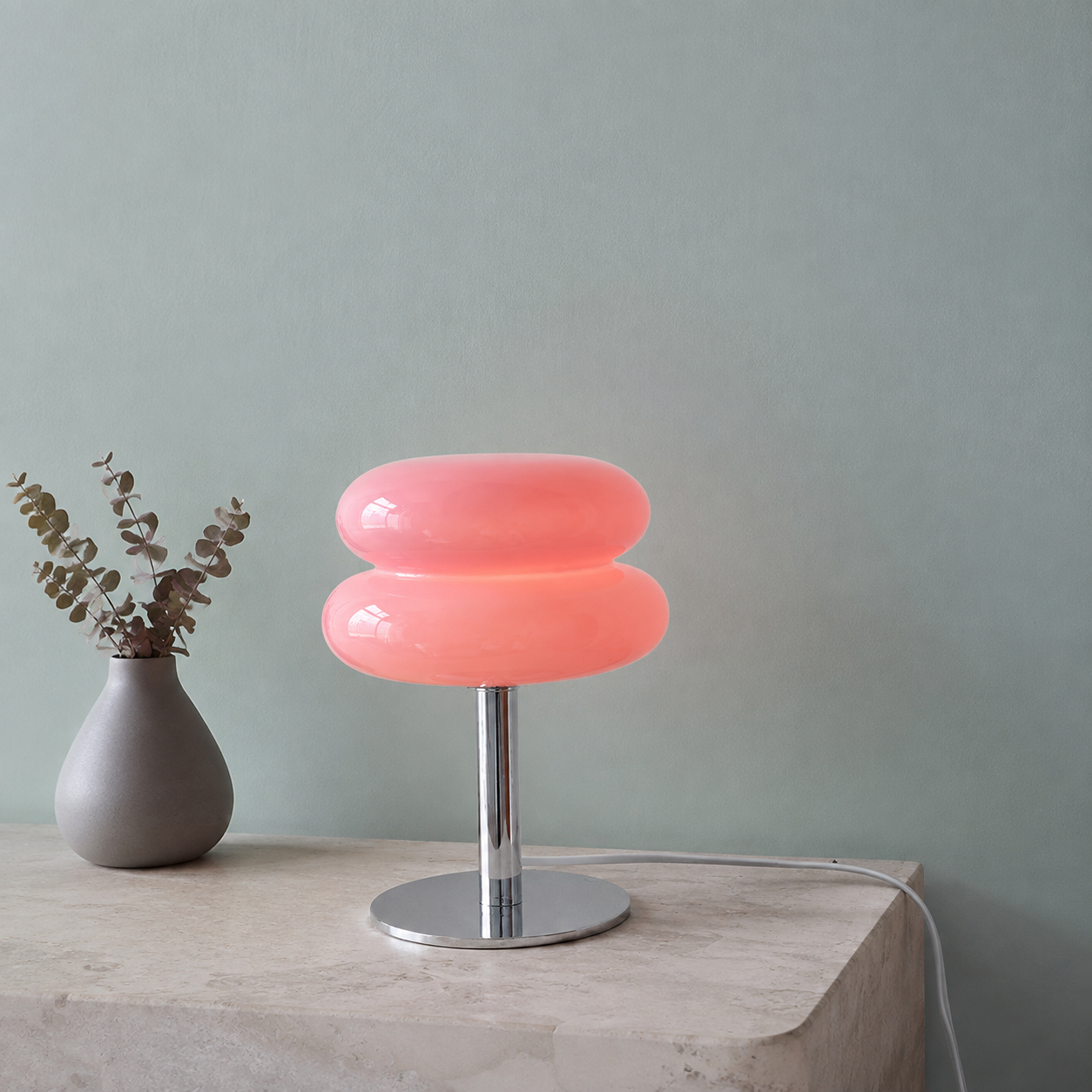 Pink sculptural glass table lamp glowing on a light quartzite console.