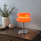 Orange sculptural glass table lamp glowing on a dark oak sideboard.