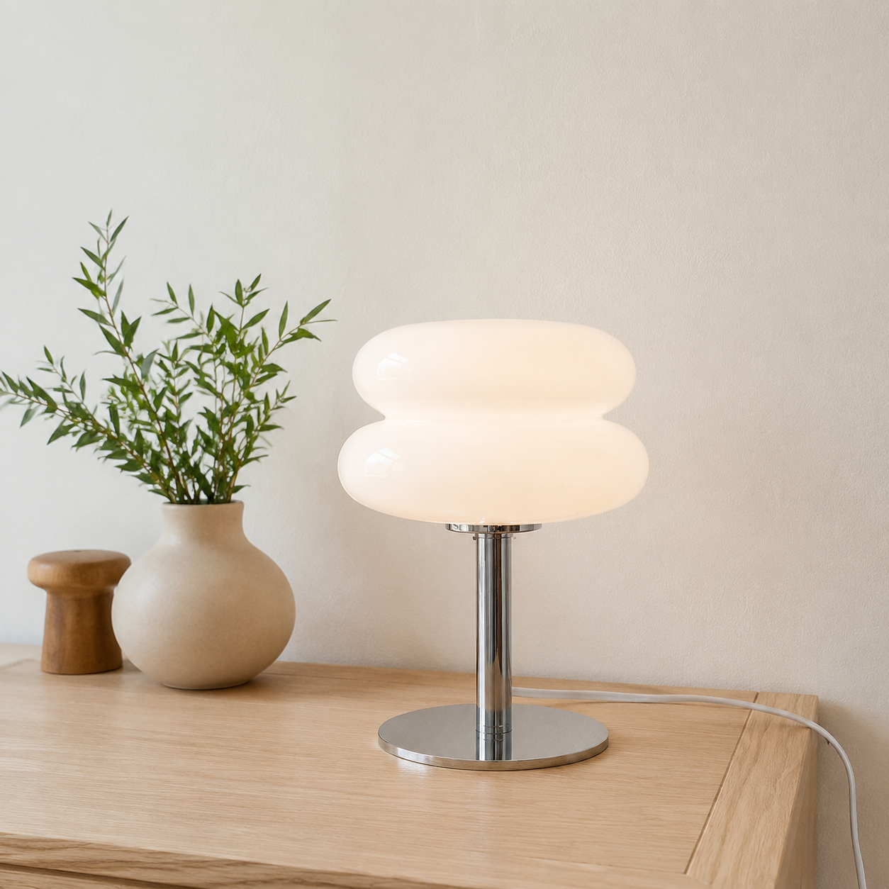White sculptural glass table lamp glowing on a pale oak console.