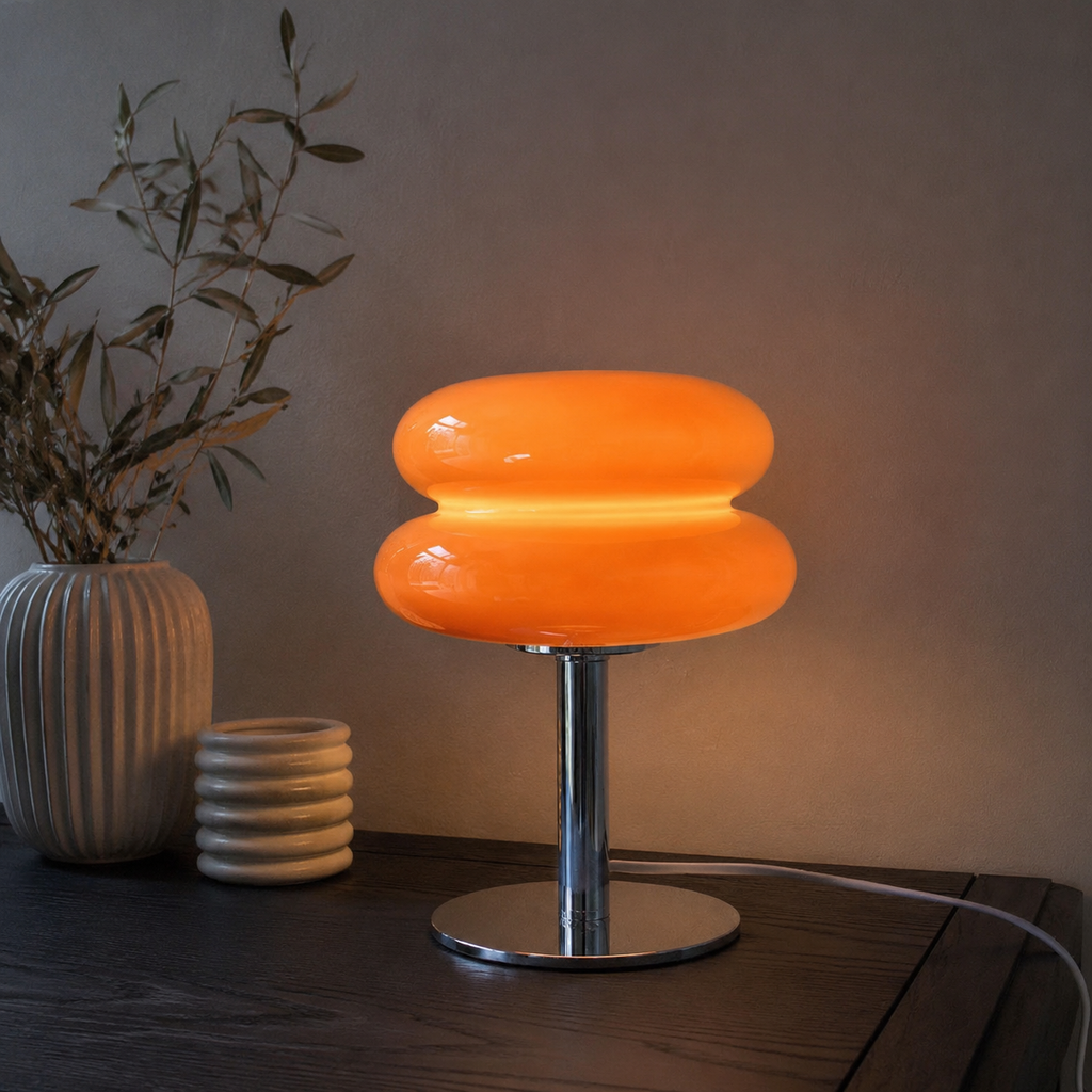 Orange sculptural glass table lamp casting warm light on a dark console.