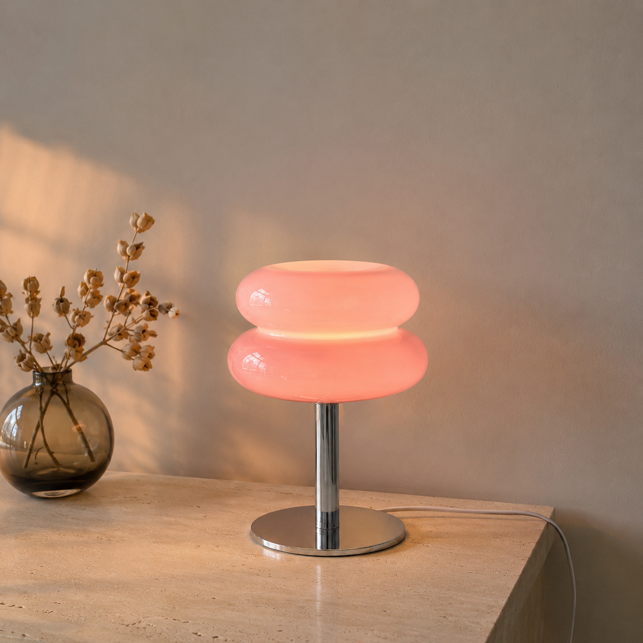 Pink sculptural glass table lamp glowing on a limestone console.