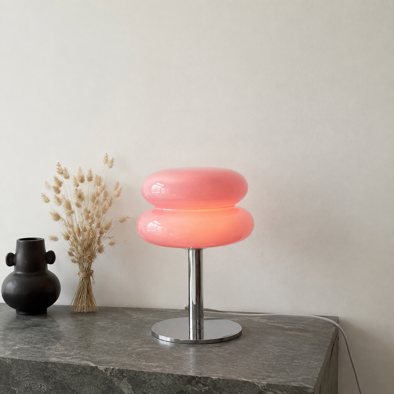Pink sculptural glass table lamp glowing on a green-gray stone console.