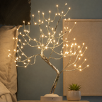 Tree of Light table lamp shown close up beside bedding and a small planter.
