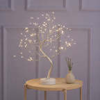 Tree of Light table lamp glowing on a round table against lavender wall trim.
