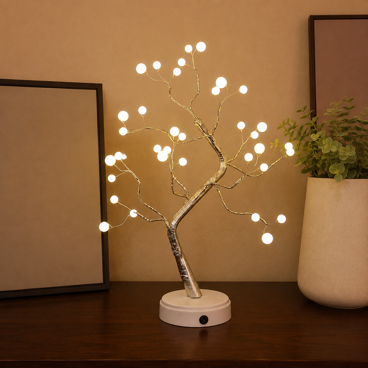 Tree of Light table lamp lit beside blank framed art and a ceramic planter.
