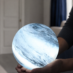 Glass moon table lamp glowing cool white while supported in two hands.
