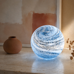 Glass moon table lamp glowing on a stone console beside a terracotta vase.