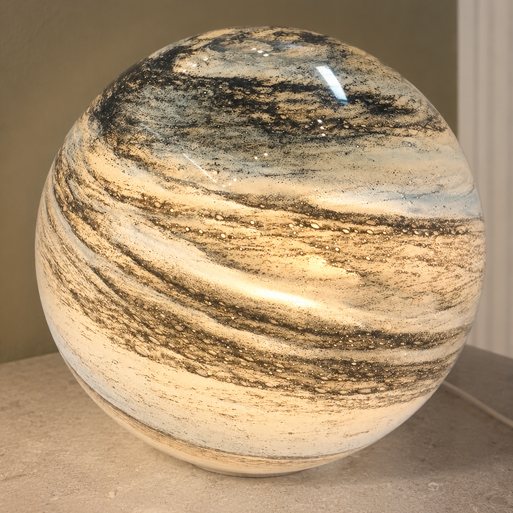 Glass moon table lamp glowing warm white in a close view on a limestone surface.